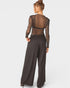 Woman wearing a brown sheer top and wide-leg pants on a white background