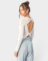 Woman wearing a white long-sleeve top with cut-out design and light blue pants on a plain background