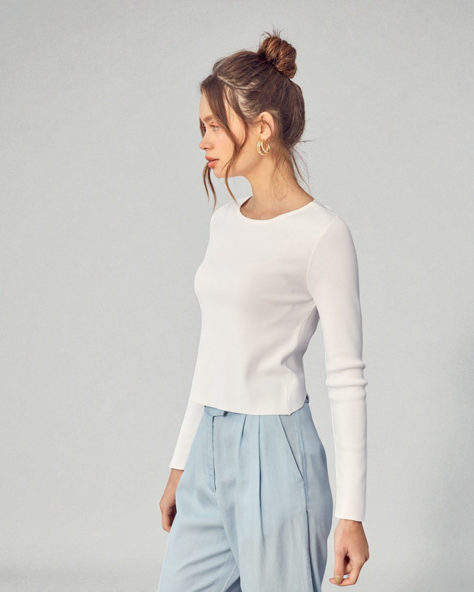 Woman wearing a white long-sleeve top and light blue pants against a gray background