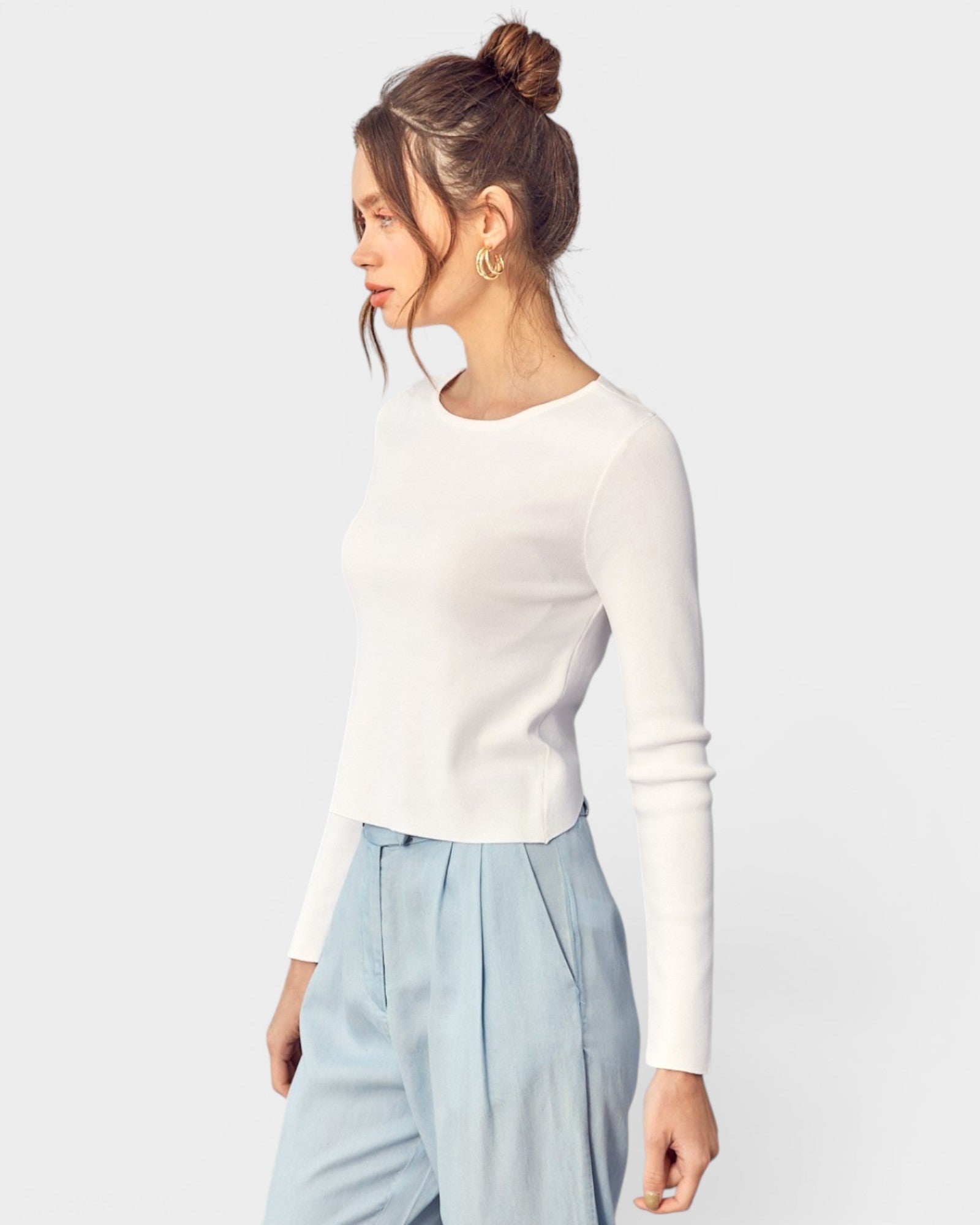 Woman wearing a white long-sleeve top and light blue pants on a plain background