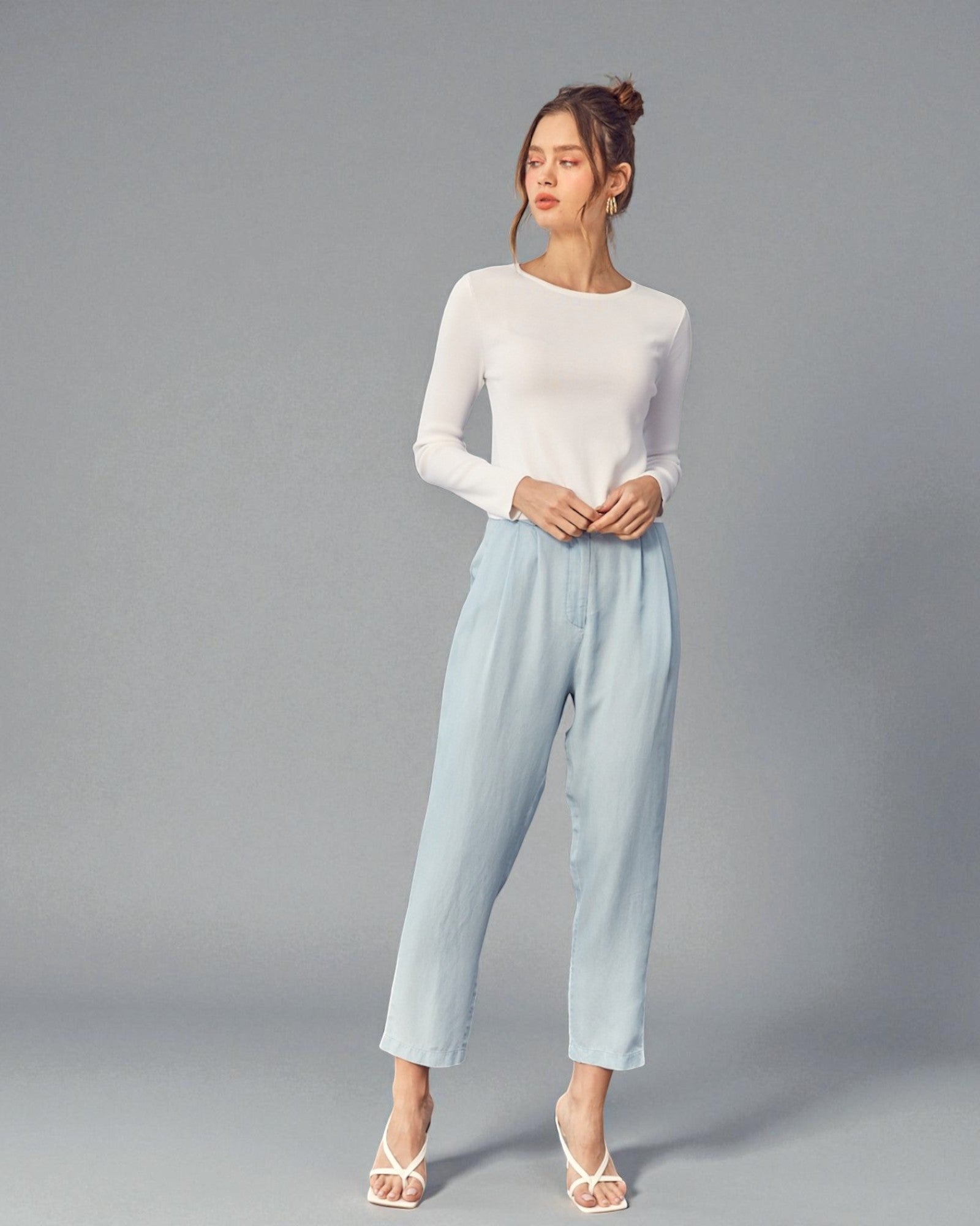 Woman wearing a white long-sleeve top and light blue pants on a gray background
