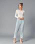 Woman wearing a white long-sleeve top and light blue pants on a gray background