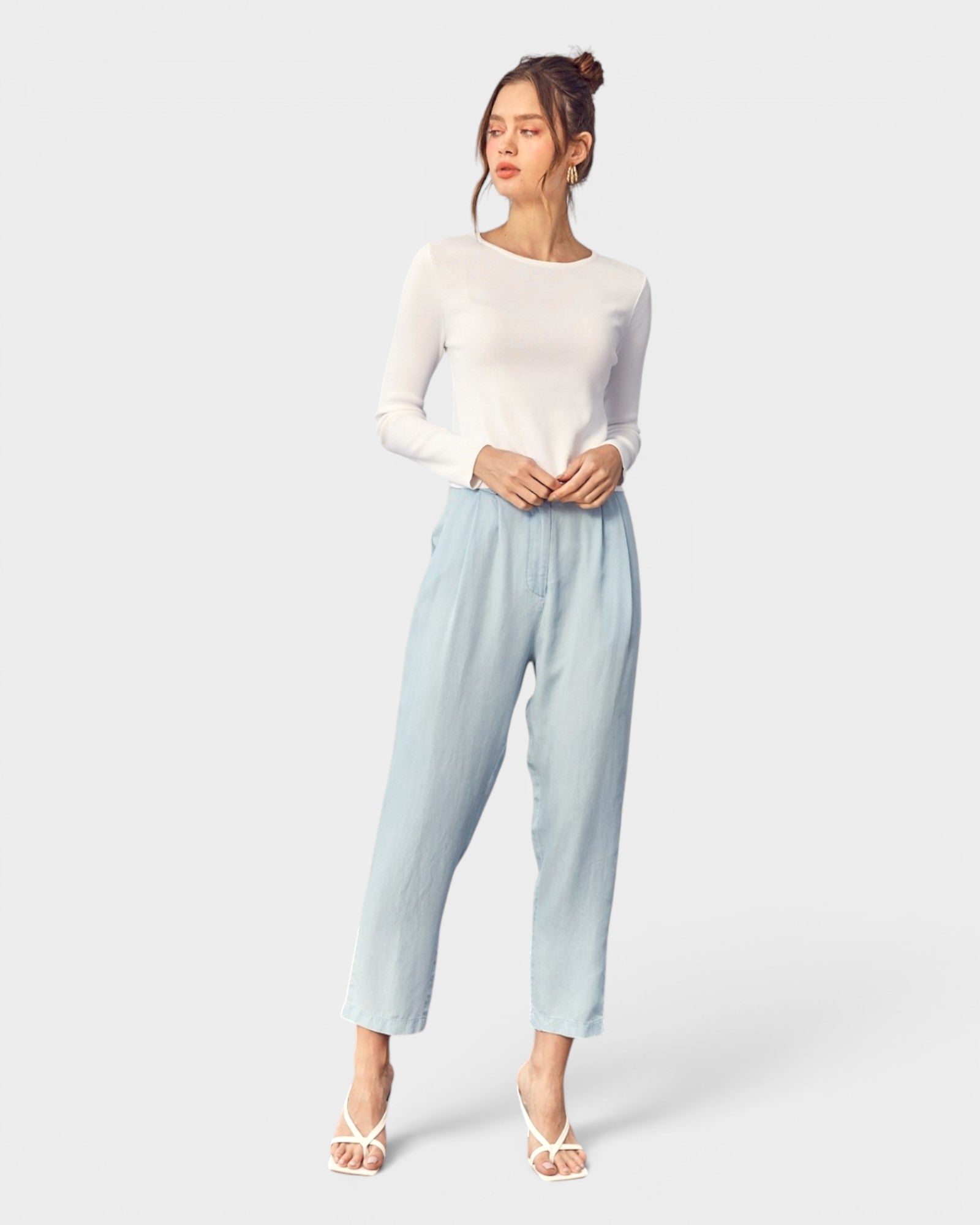 Woman wearing a white long-sleeve top and light blue pants on a white background