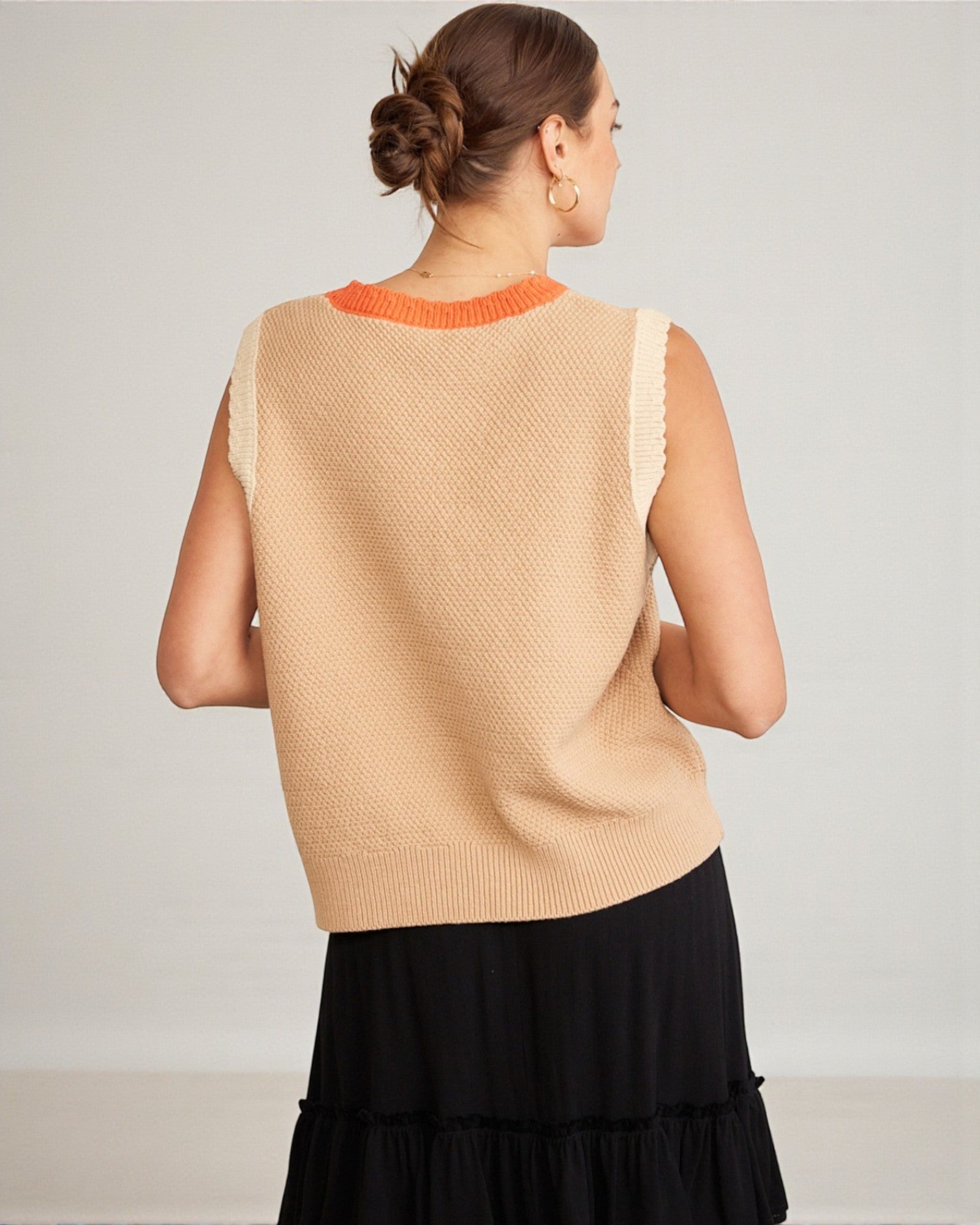 Woman wearing a beige sleeveless top with orange trim on a plain background