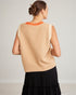 Woman wearing a beige sleeveless top with orange trim on a plain background