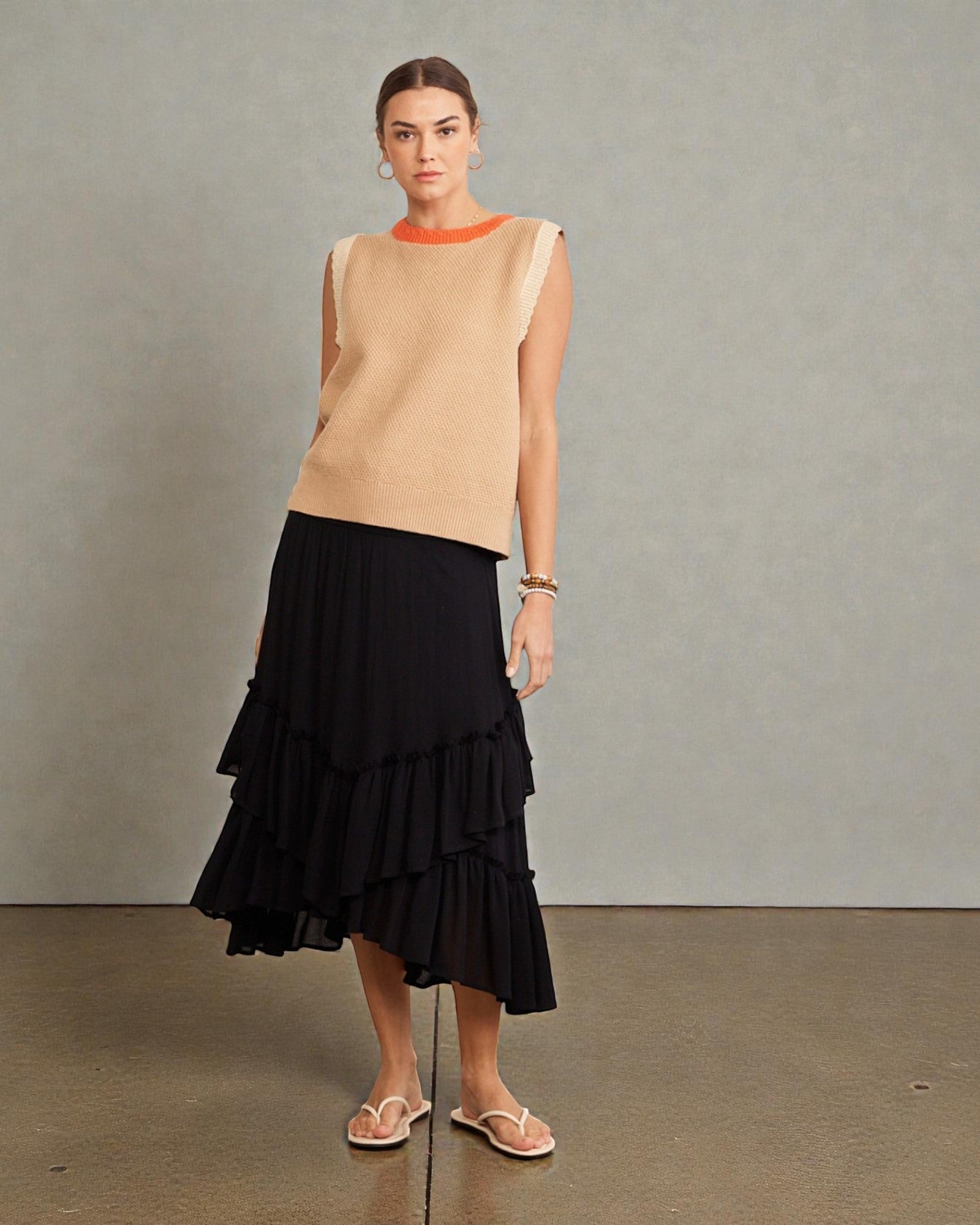 Woman wearing a beige sleeveless top and black ruffled skirt against a plain background