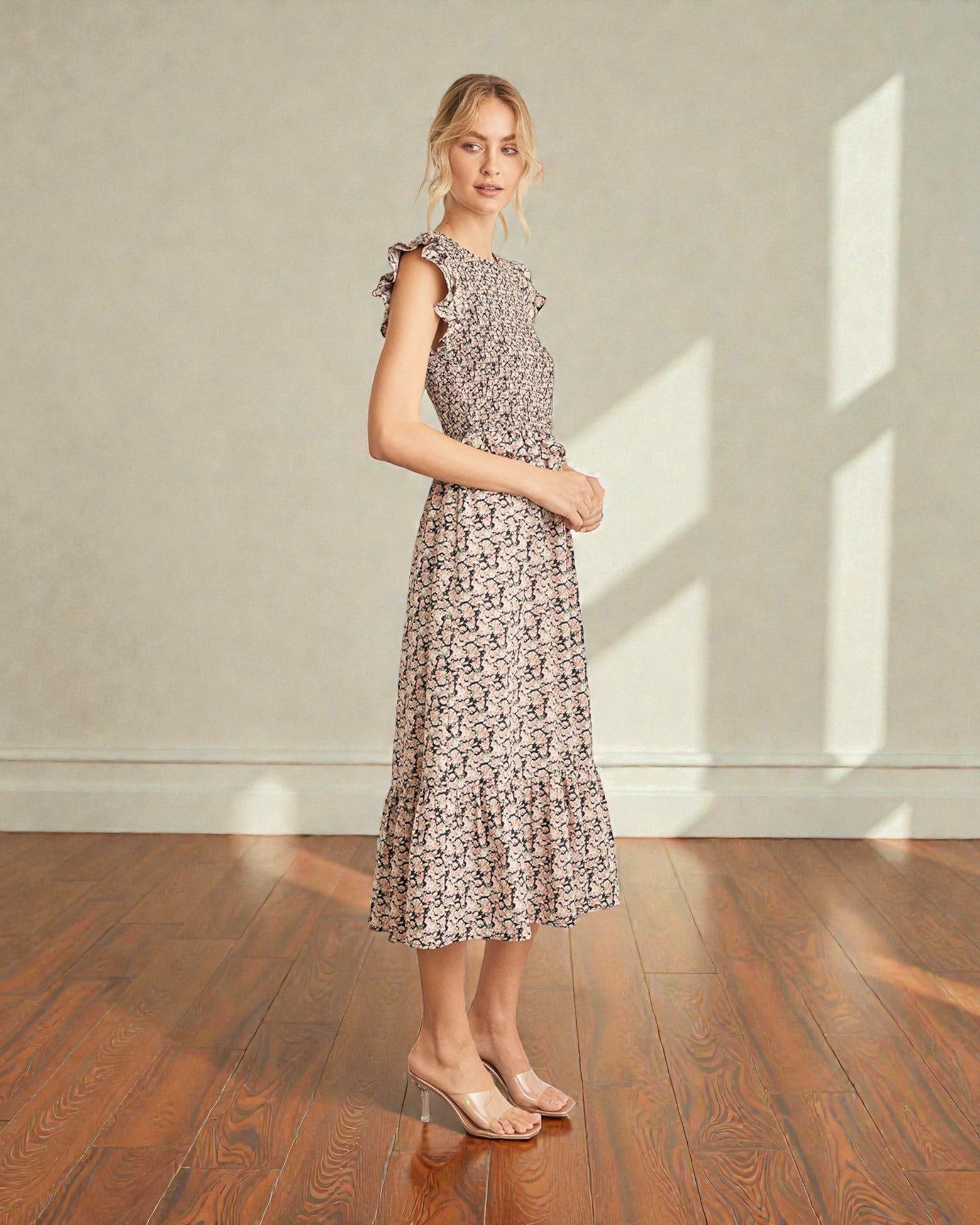Woman wearing a floral dress standing in a room with wooden flooring and a neutral wall.