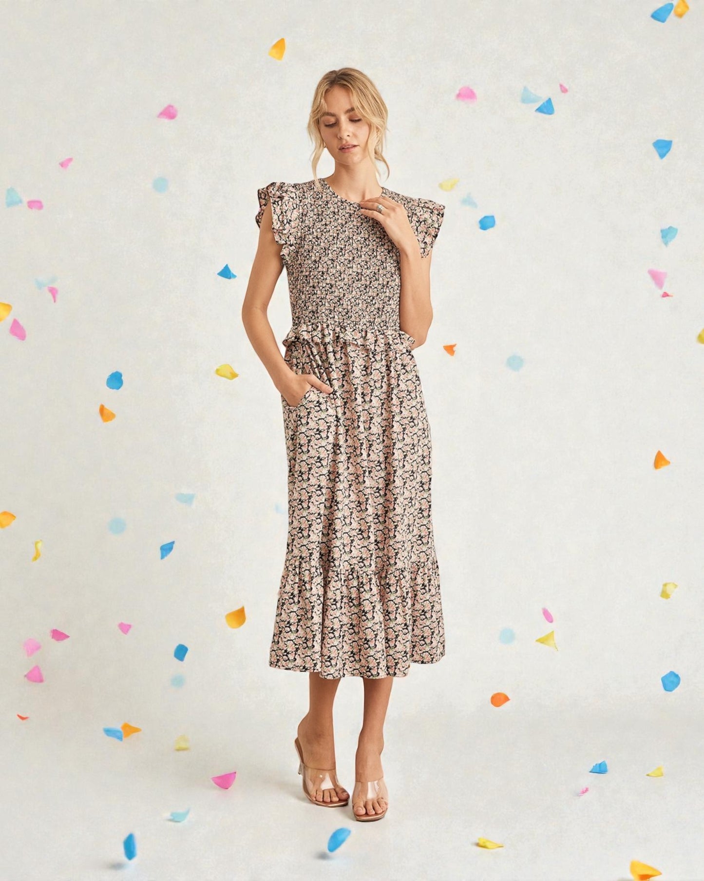 Woman wearing a floral dress against a light background with colorful confetti-like shapes.