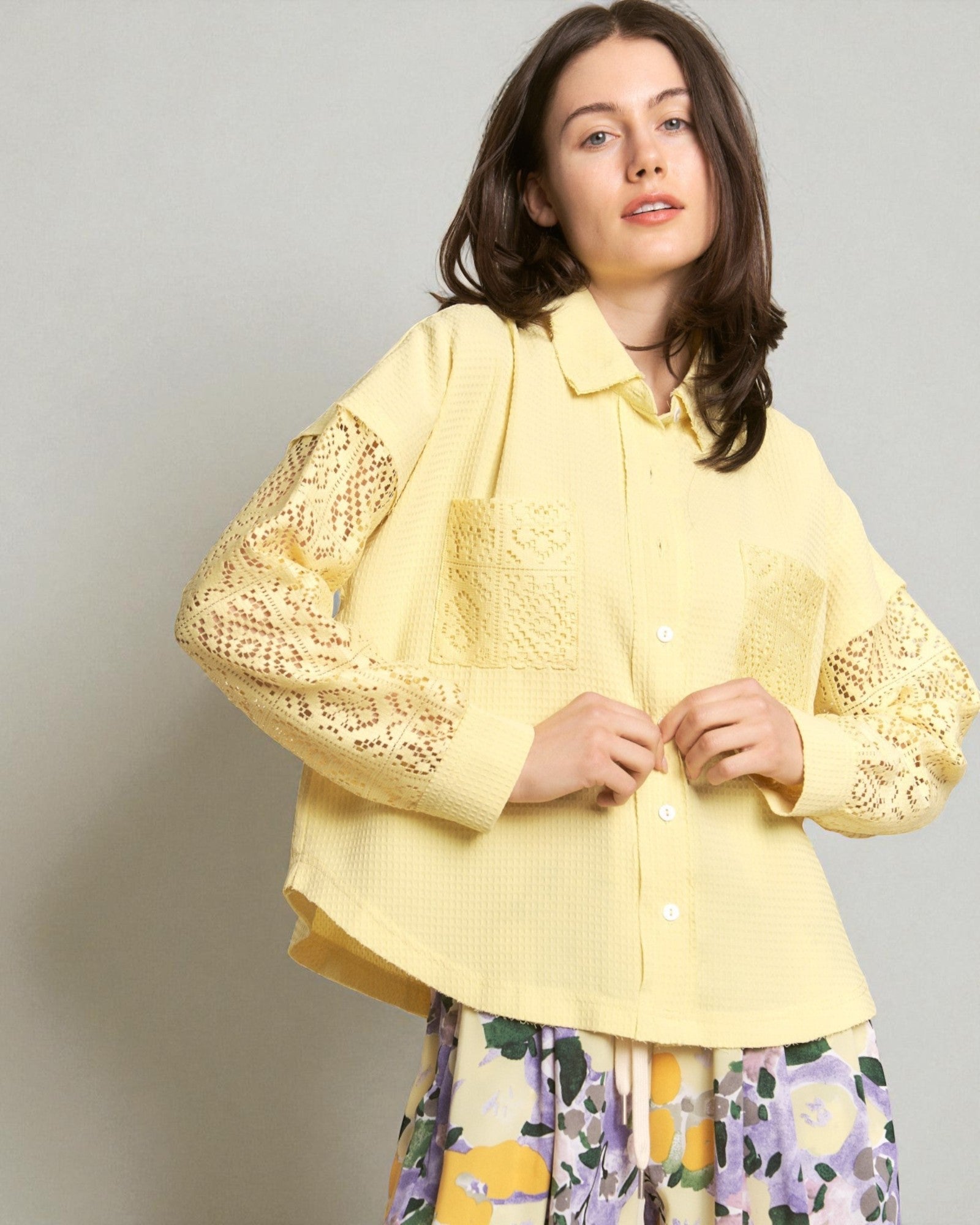 Woman wearing a yellow lace-trimmed shirt against a plain background