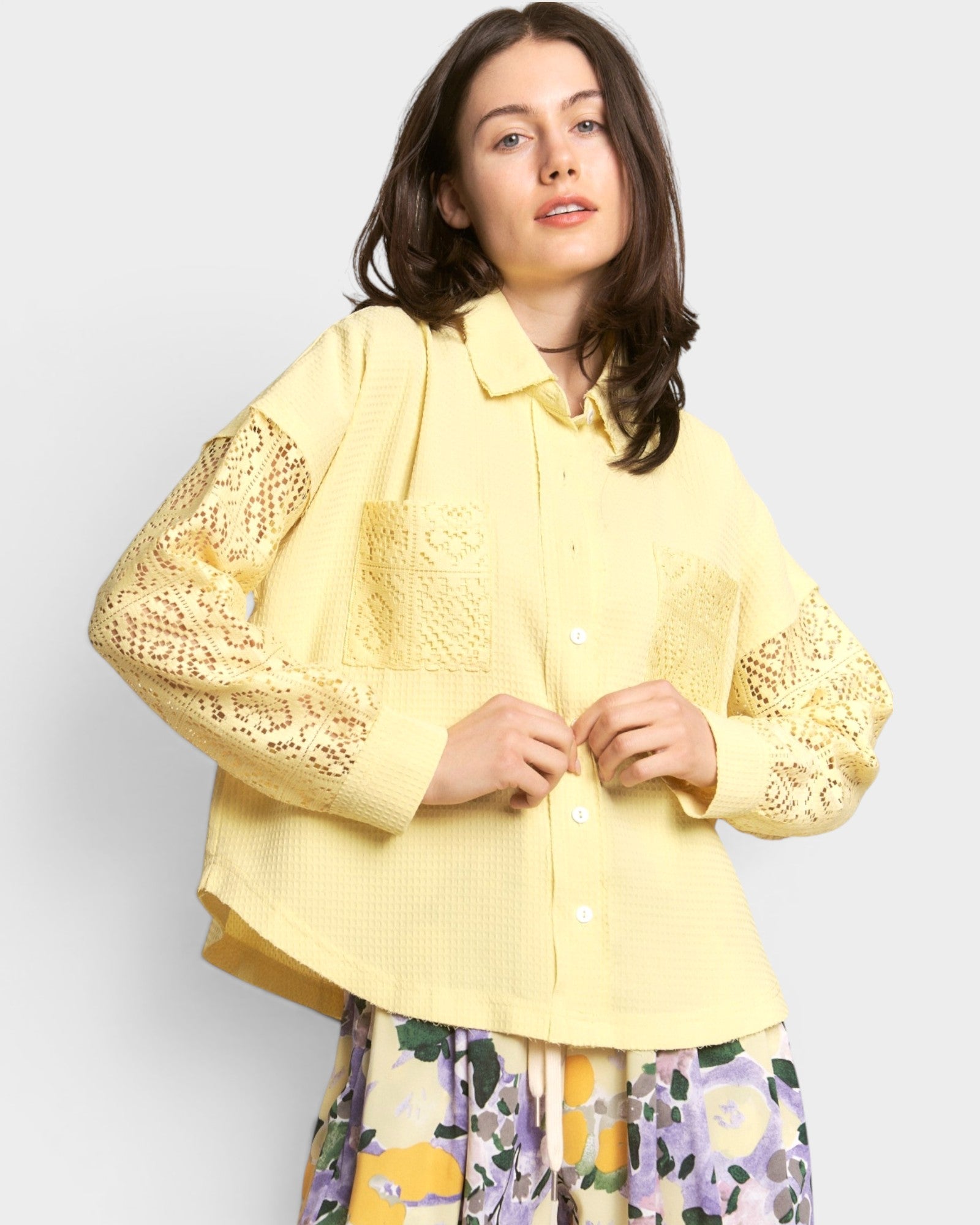 Woman wearing a yellow shirt with lace sleeves against a white background