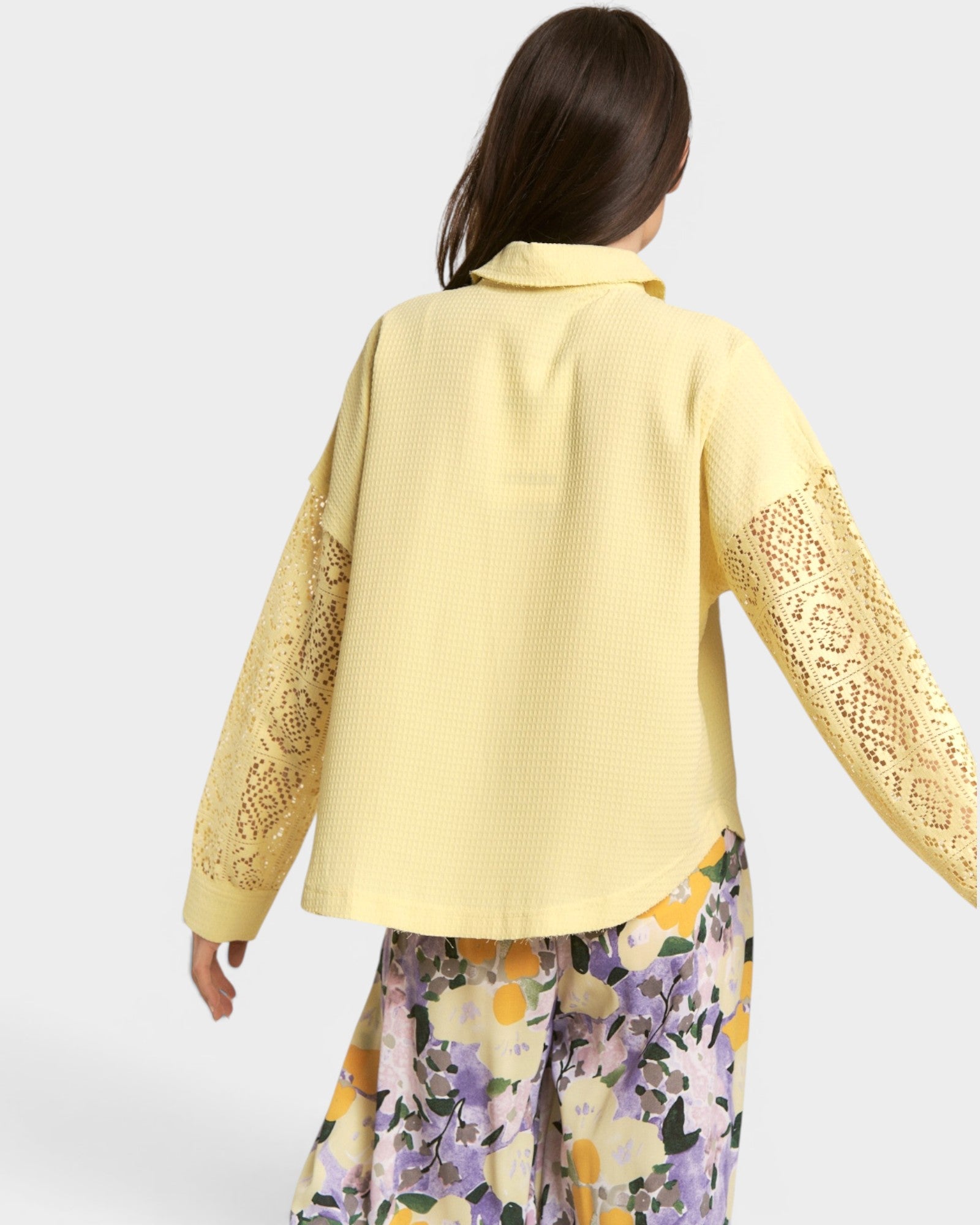 Woman wearing a yellow embroidered jacket with floral pants on a white background