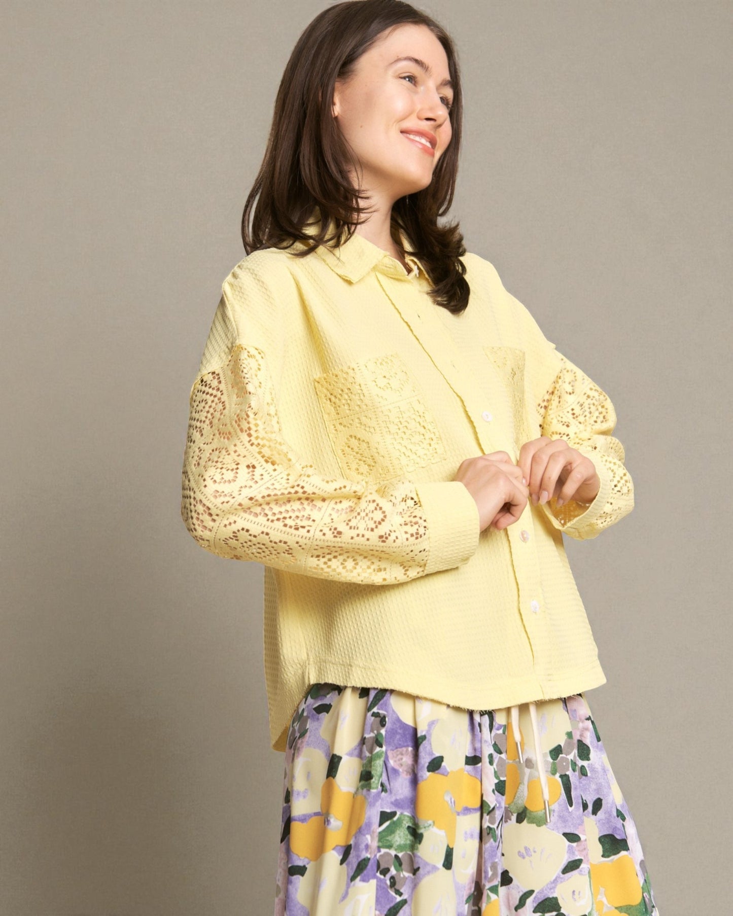 Woman wearing a yellow lace top with a floral skirt against a plain background