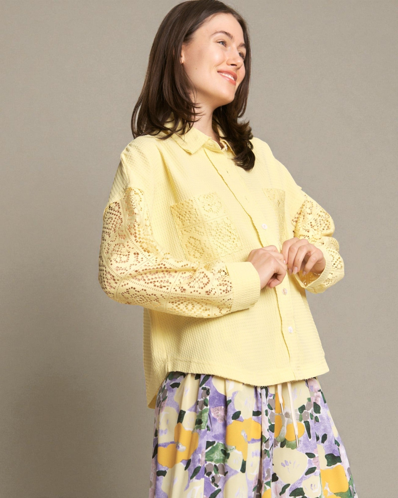 Woman wearing a yellow lace top with a floral skirt against a plain background