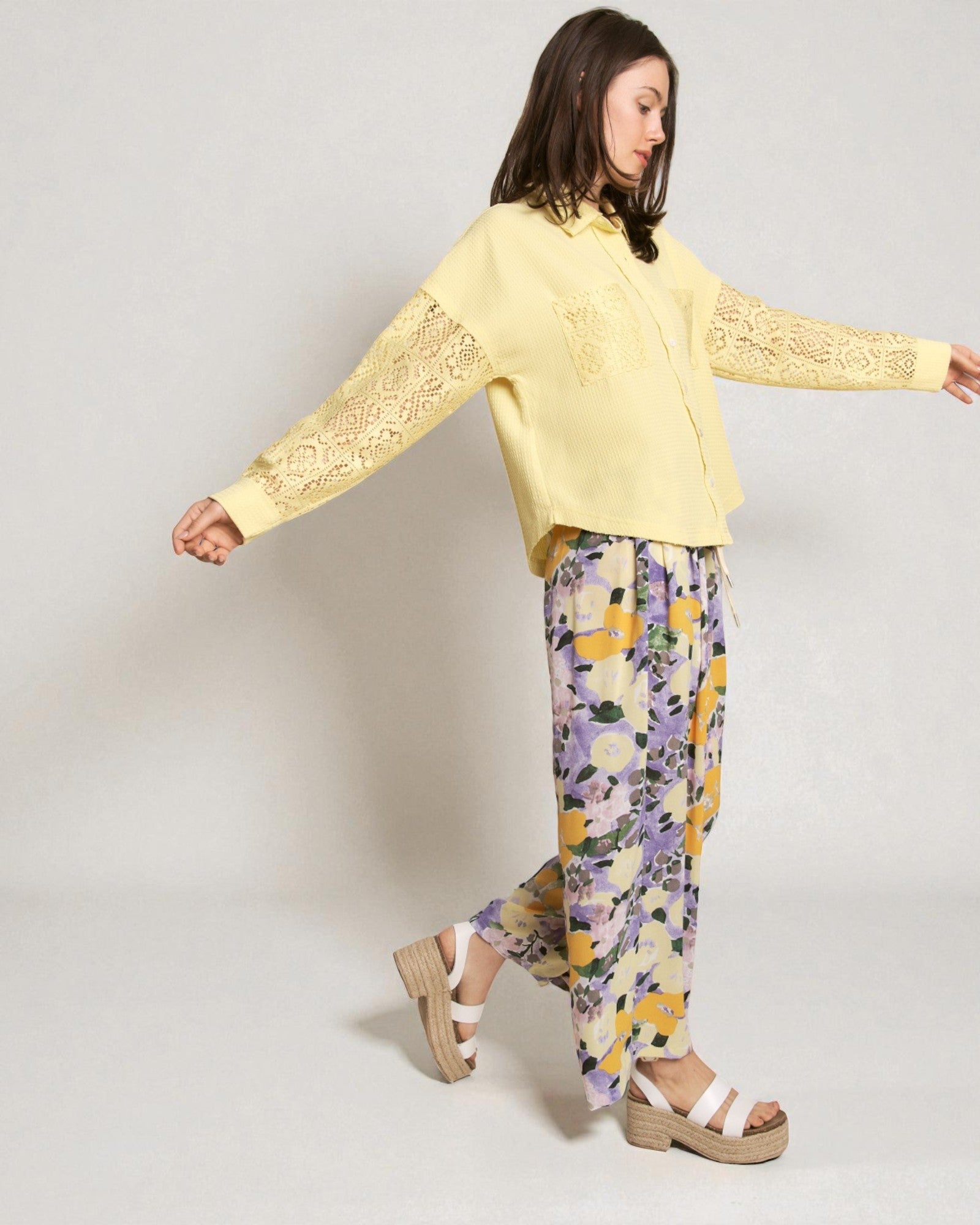 Woman wearing a yellow top with lace sleeves and floral pants on a plain background