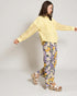 Woman wearing a yellow top with lace sleeves and floral pants on a plain background