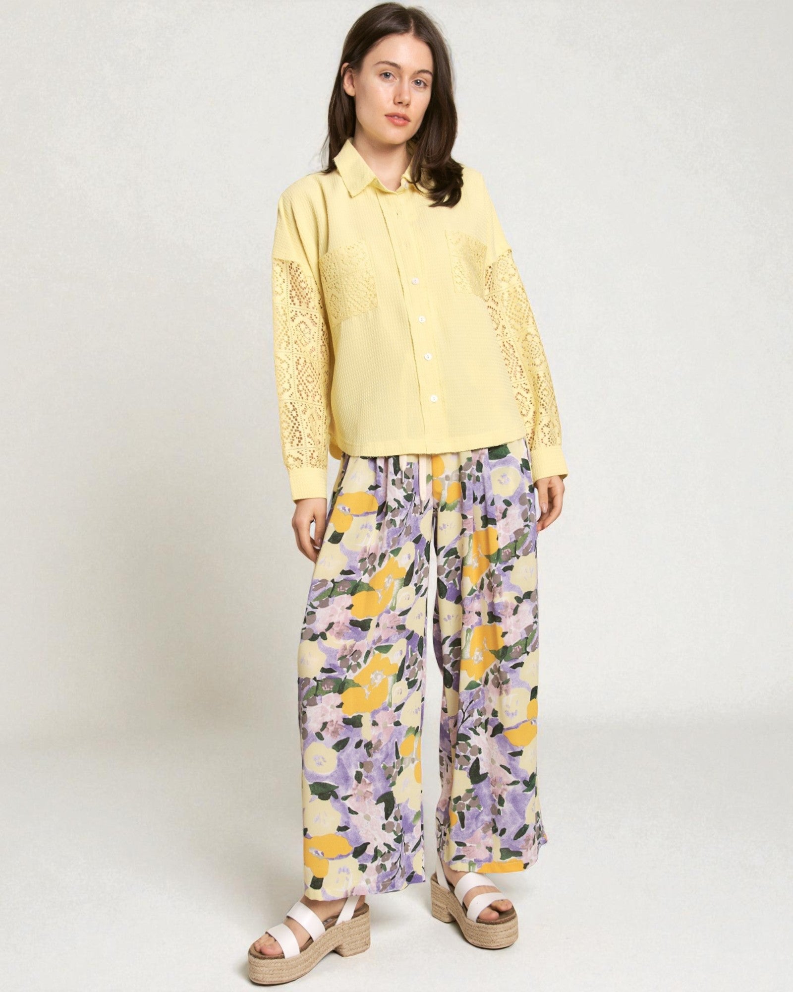 Woman wearing a yellow lace blouse and floral pants on a white background