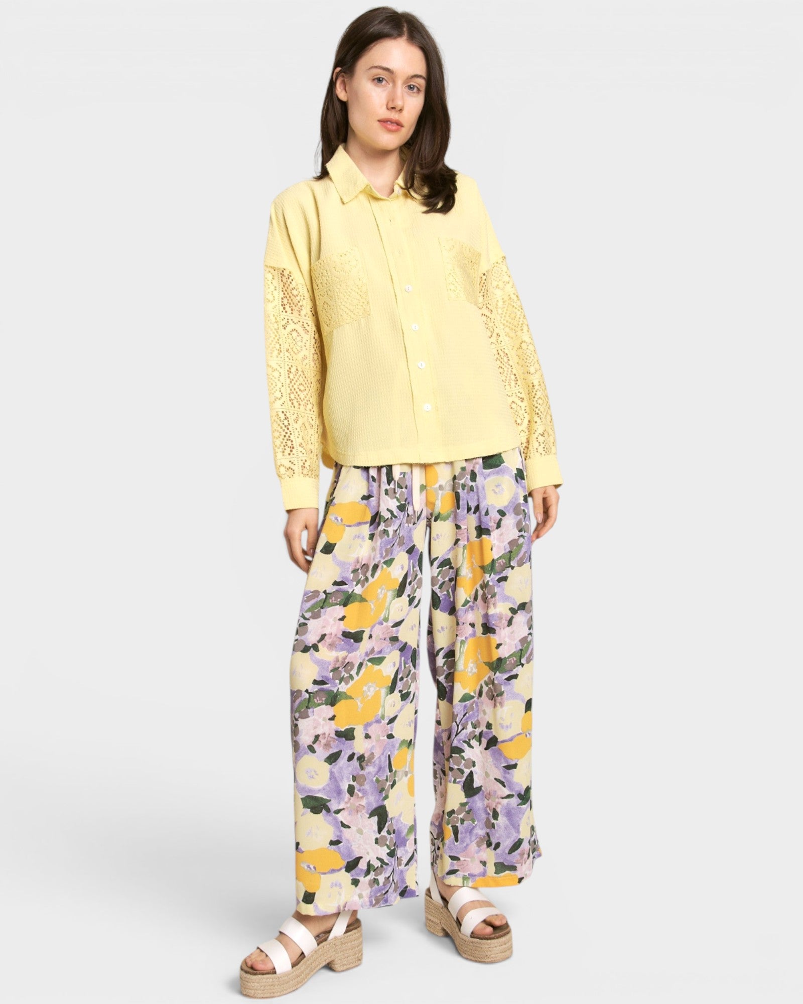 Woman wearing a yellow lace top and floral pants on a white background
