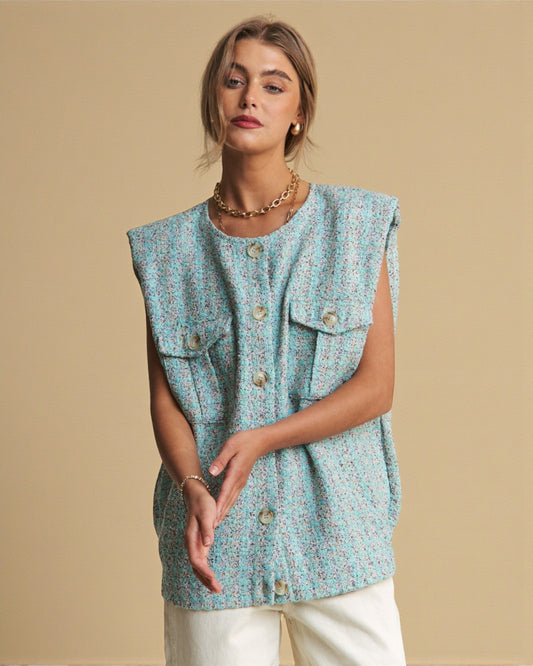 Woman wearing a light blue sleeveless top with button details against a beige background