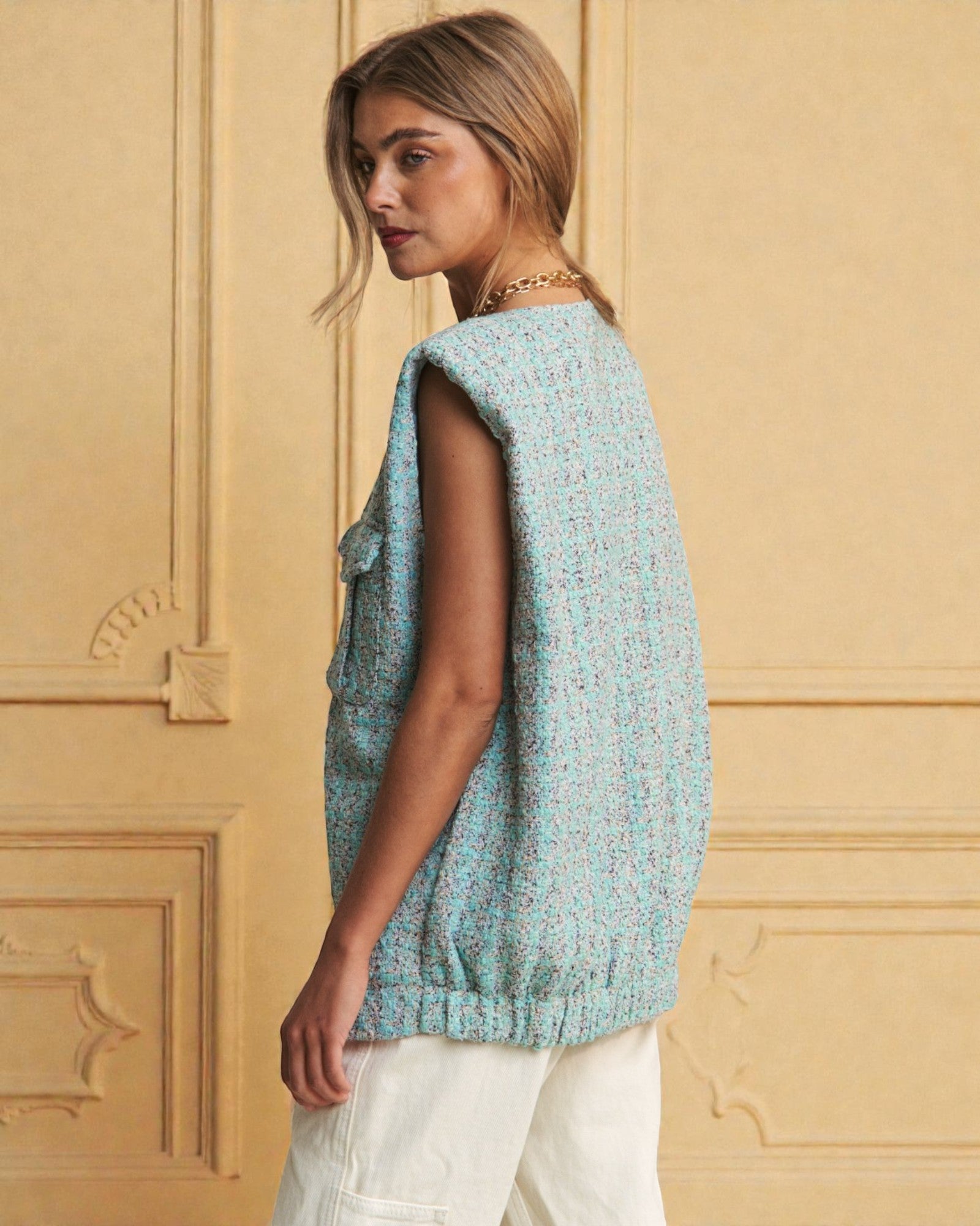 Woman wearing a light blue sleeveless top against a yellow wall