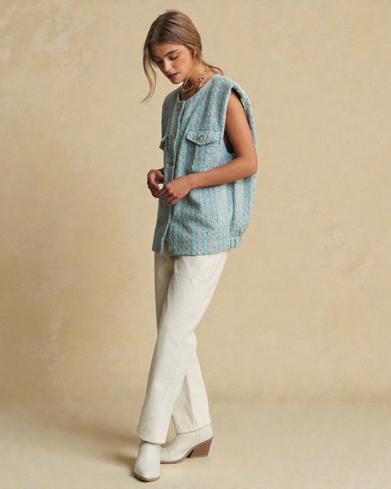 Woman wearing a sleeveless blue top and white pants against a beige background