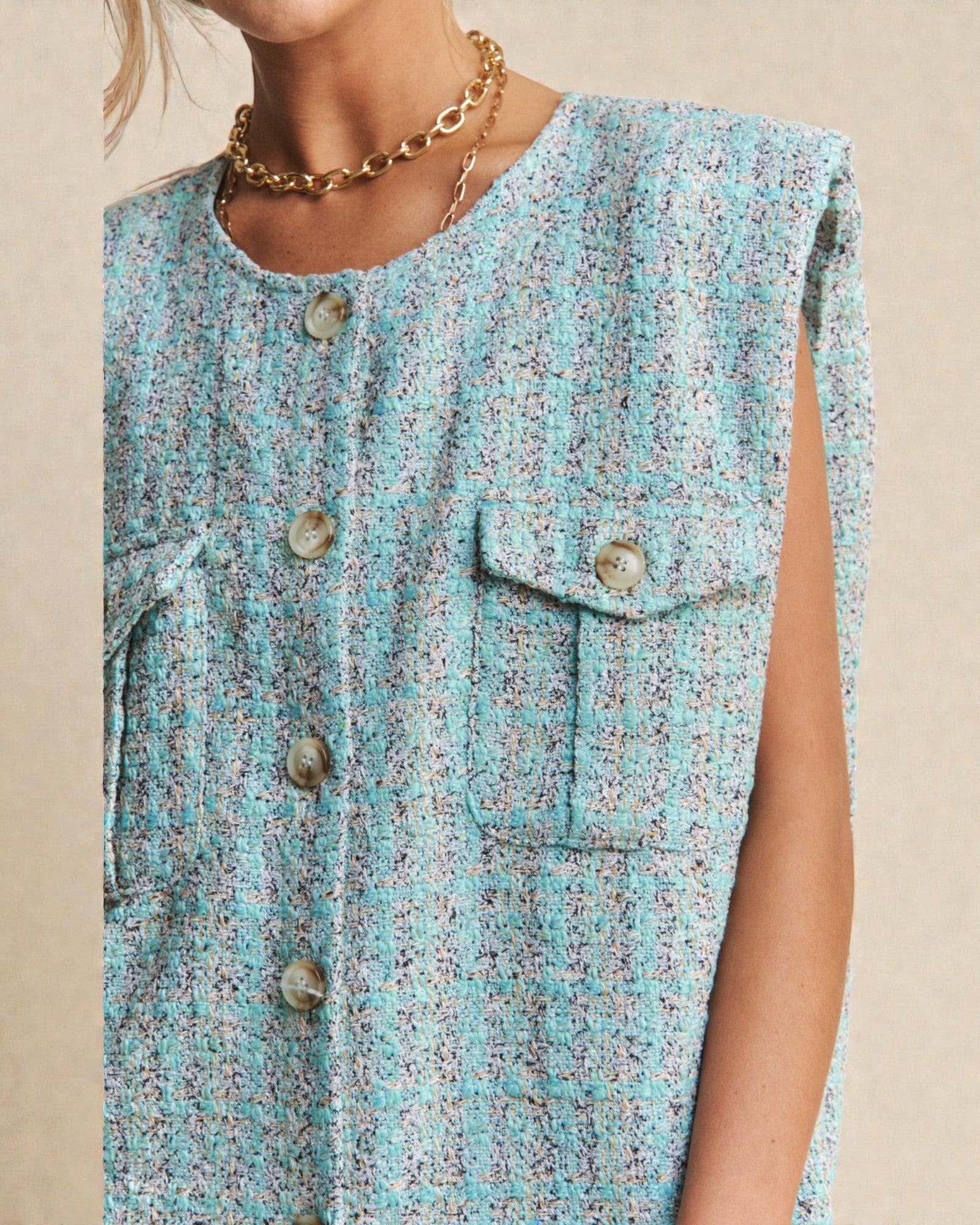 Teal floral sleeveless top with buttons on a beige background
