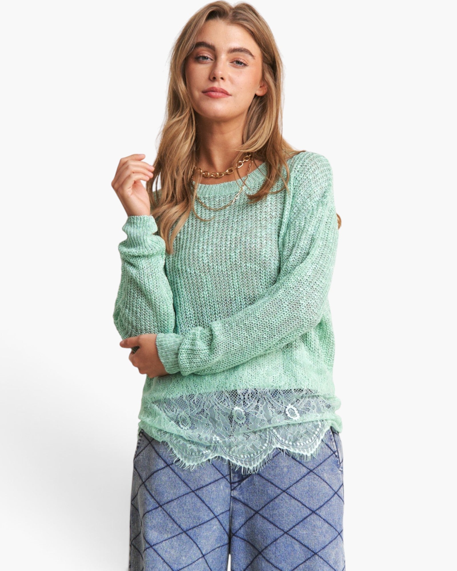 A woman wearing a mint green fuzzy knit sweater with a scalloped lace hem, paired with blue diamond-patterned pants, against a plain white studio background.