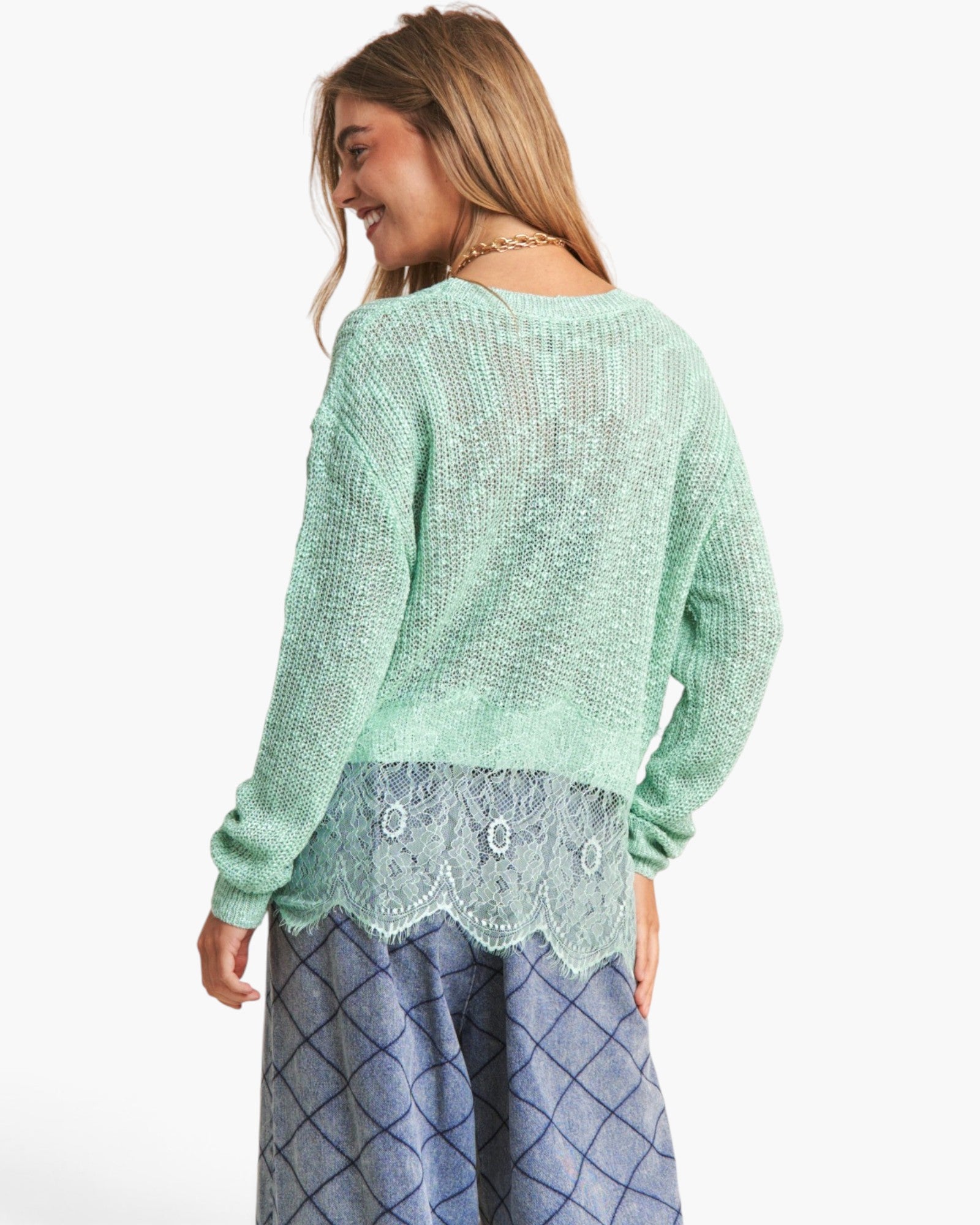 A woman shown from the back wearing a mint green textured knit sweater layered over a blue patterned skirt with a lace hem detail, against a plain white background.