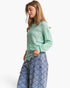 A woman wearing a light mint green knit sweater and blue patterned wide-leg jeans, photographed against a clean white studio background.