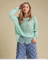 Woman wearing a light green sweater and blue plaid pants against a beige background