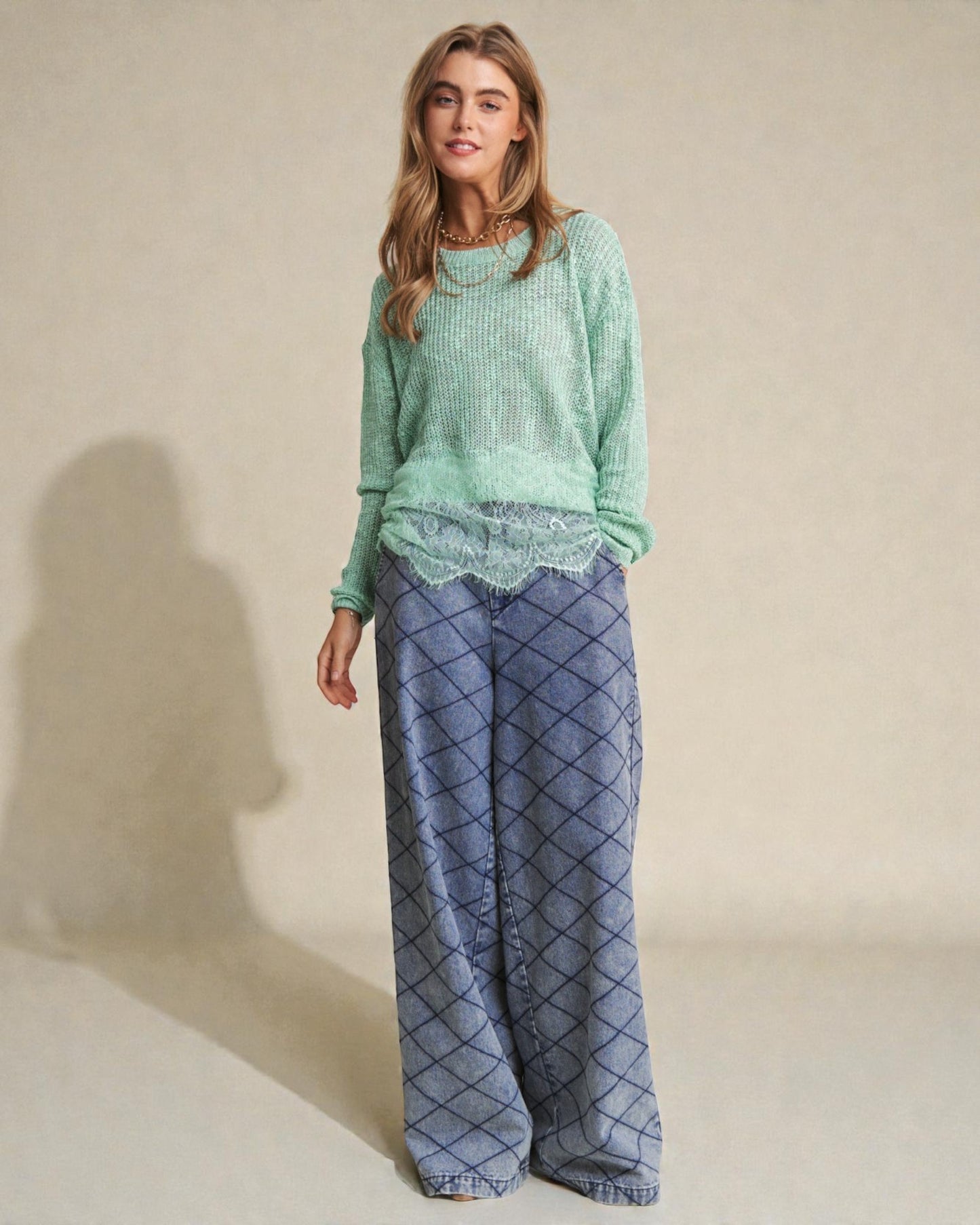 Woman wearing a green sweater and blue patterned pants on a beige background