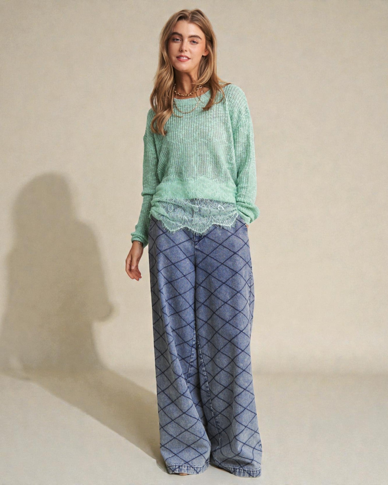 Woman wearing a green sweater and blue patterned pants on a beige background