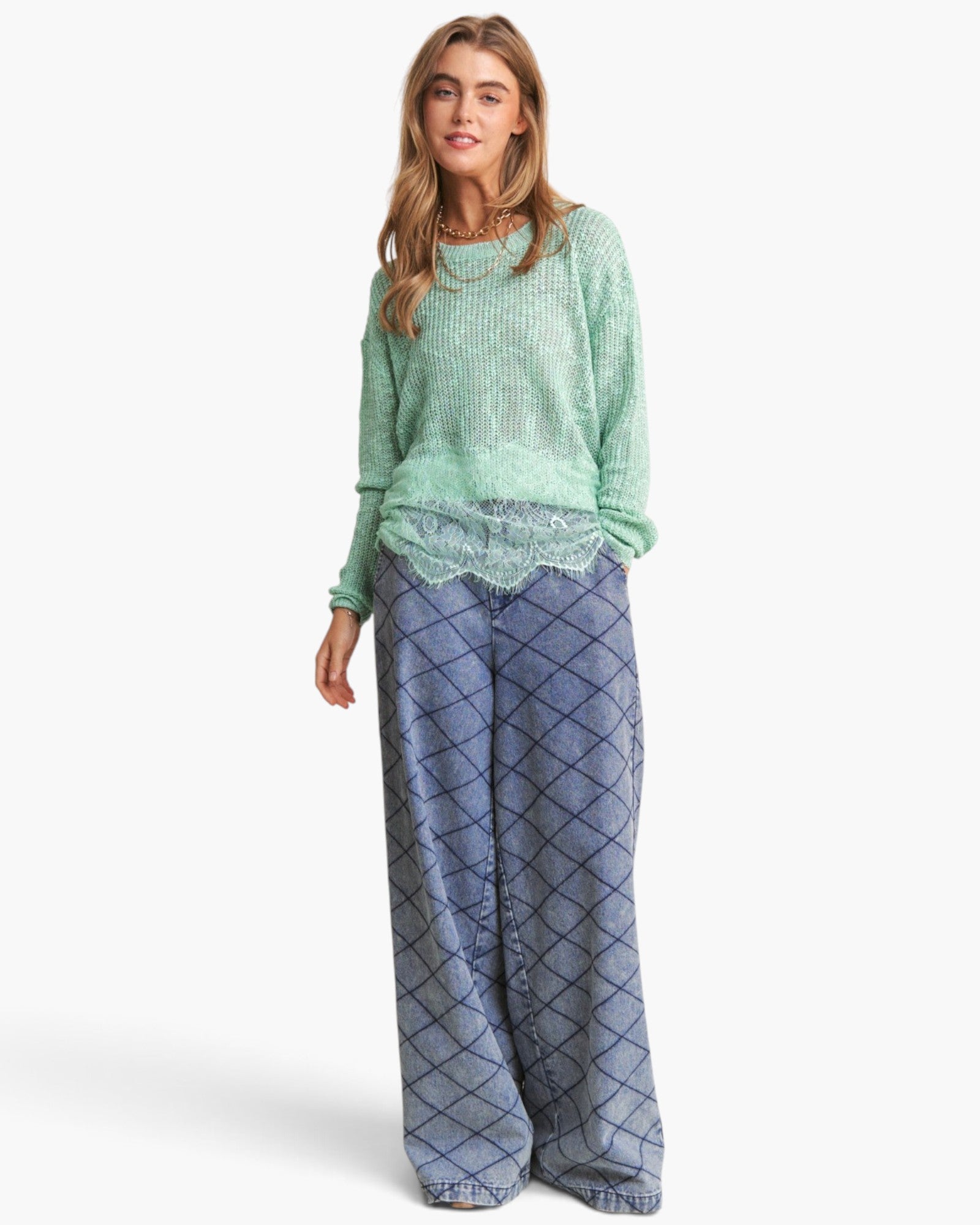 A woman modeling a light green knit sweater and blue wide-leg pants with a dark diamond pattern, set against a plain white studio background.