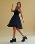 Woman in a black dress and platform shoes posing against a beige background