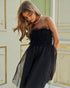 Woman wearing a black strapless dress with floral details in an elegant interior setting.