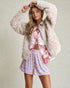 Woman wearing a fluffy white cardigan, tie-dye shirt, and sequin shorts on a plain background