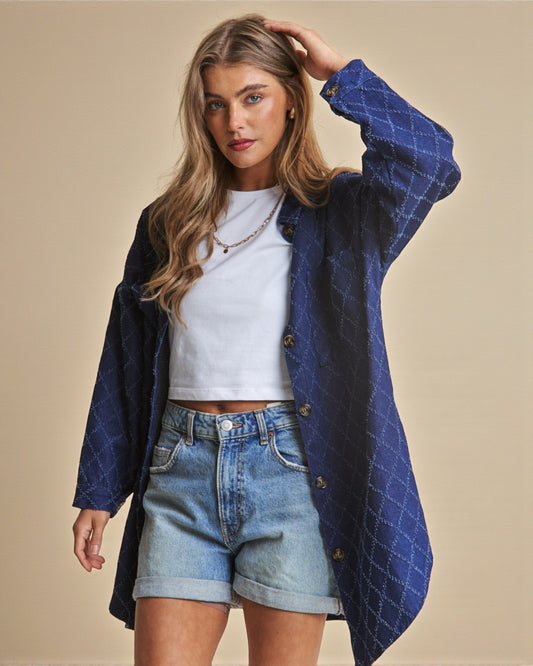 Woman wearing a blue quilted coat over a white top and denim shorts on a beige background