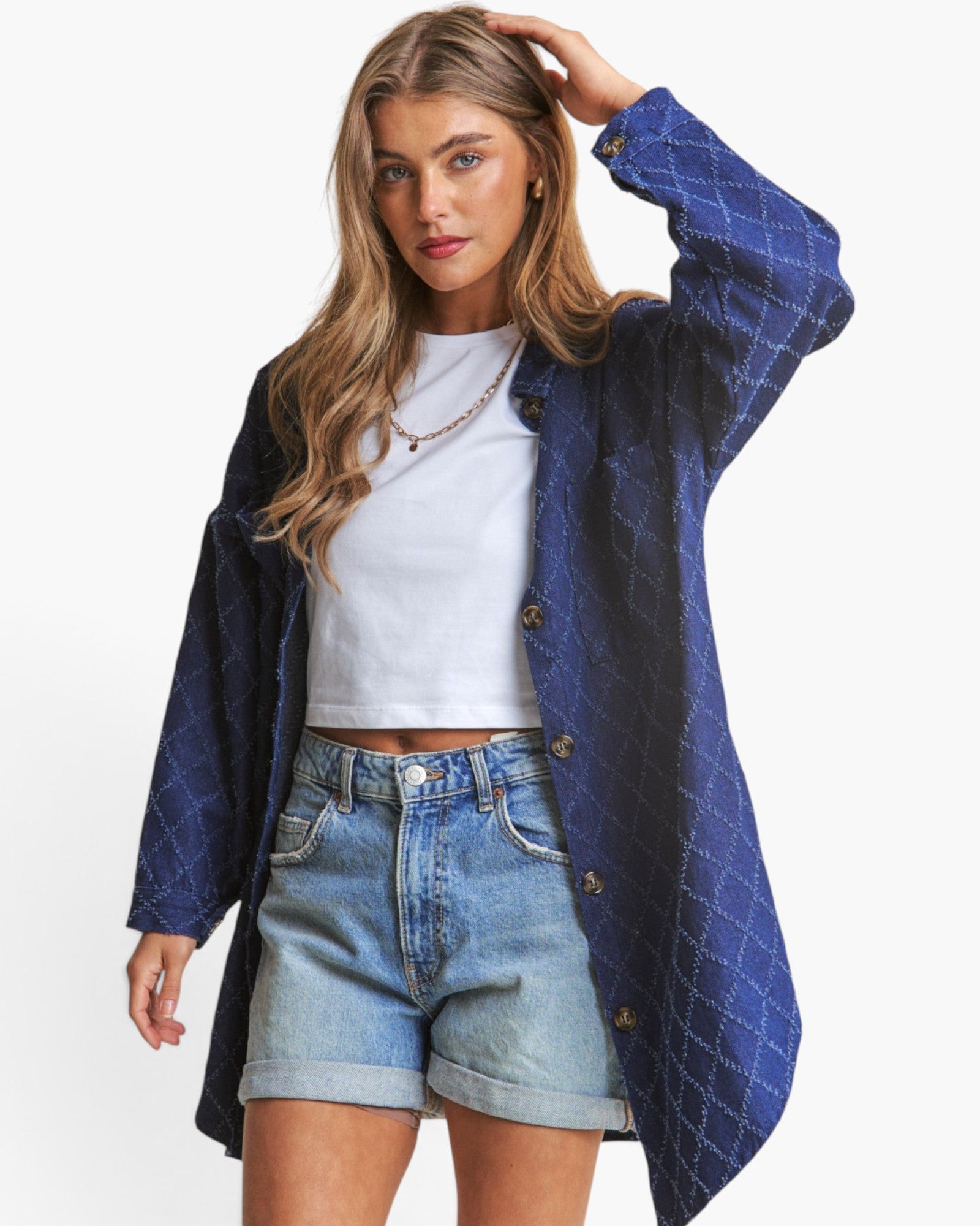 A woman modeling a blue patterned button-up shirt jacket over a white crop top and light-wash denim shorts against a plain white background.