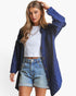 A woman modeling a blue patterned button-up shirt jacket over a white crop top and light-wash denim shorts against a plain white background.