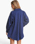 A woman shown from the back wearing a blue button-up shirt with a subtle diamond pattern, photographed against a clean white studio background.