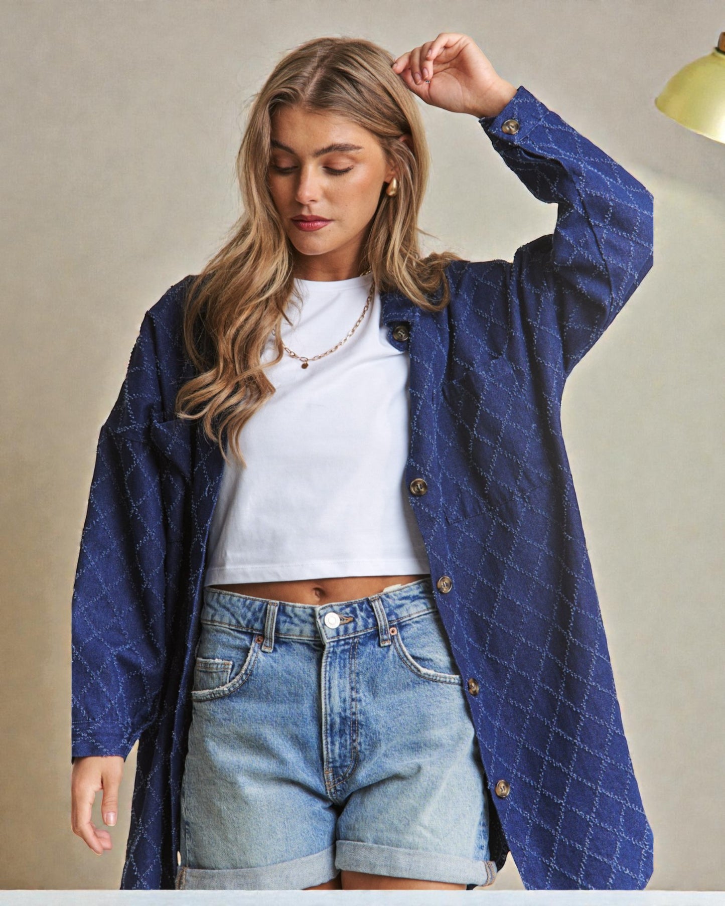 Woman wearing a blue plaid shirt over a white top and denim shorts on a beige background
