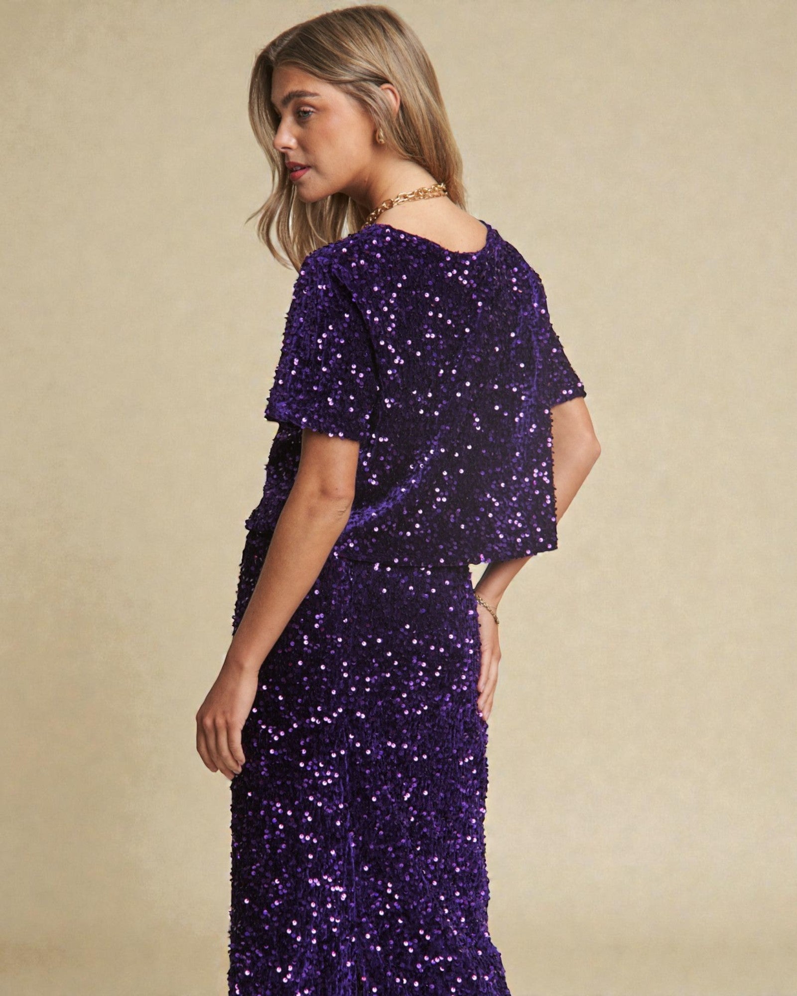 Woman wearing a purple sequin dress against a beige background