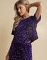 Woman wearing a purple sequin dress against a beige background