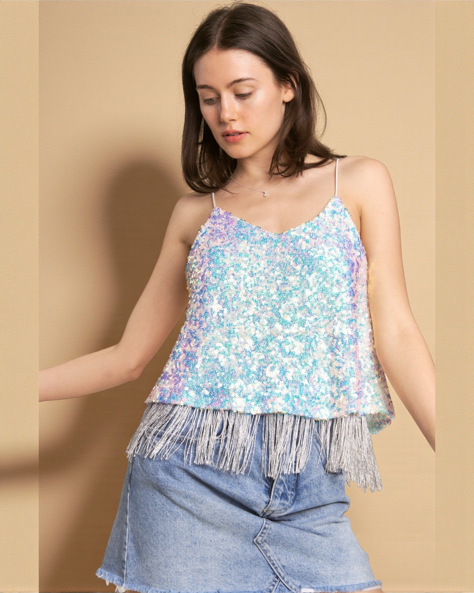 Woman wearing a sequin top with fringe and denim shorts on a beige background