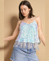 Woman wearing a sequin top with fringe and denim shorts on a beige background