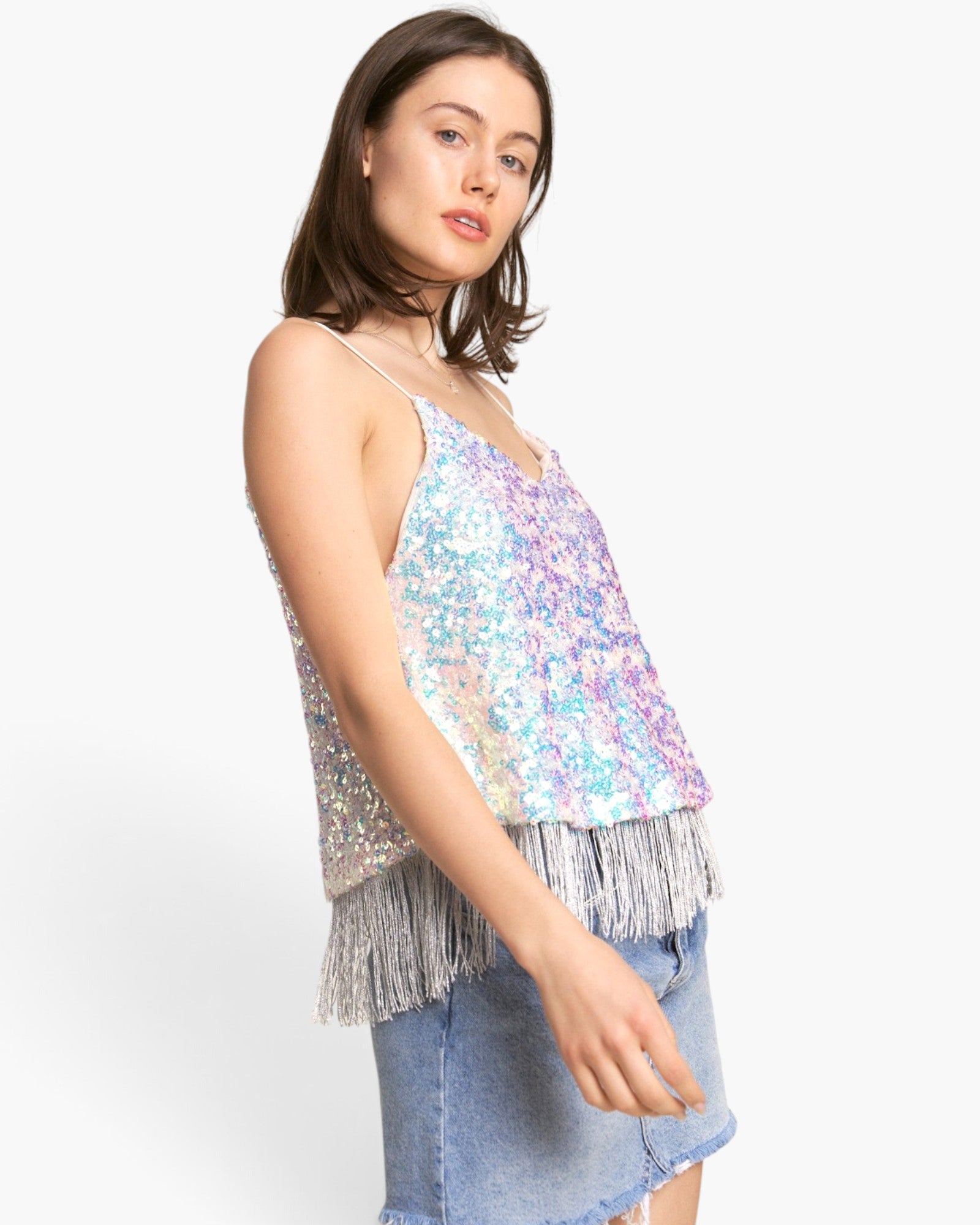 A woman modeling a sleeveless sequined camisole top with silver fringe, paired with a denim skirt, against a plain light gray studio background.