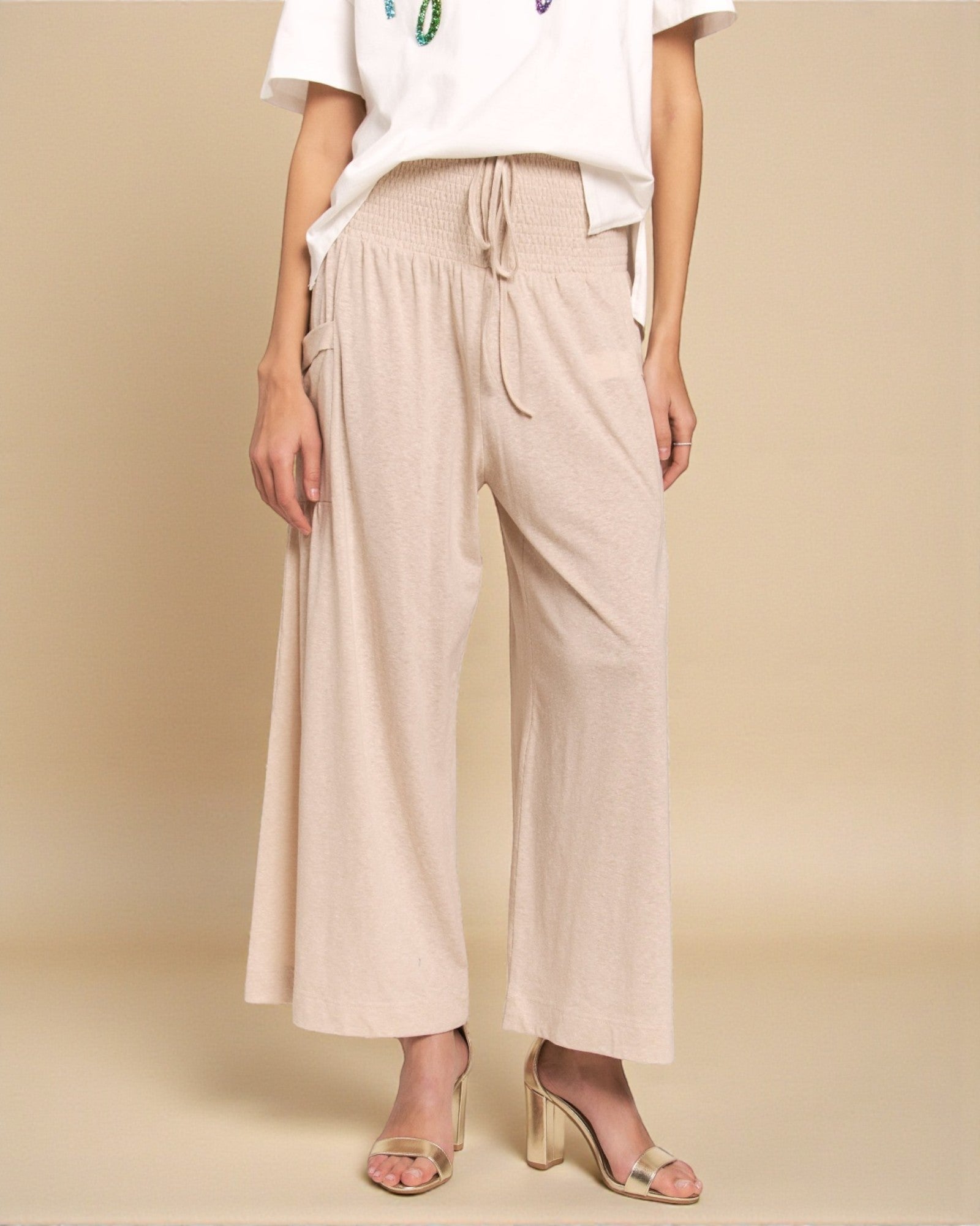 Person wearing beige wide-leg pants and a white top on a beige background