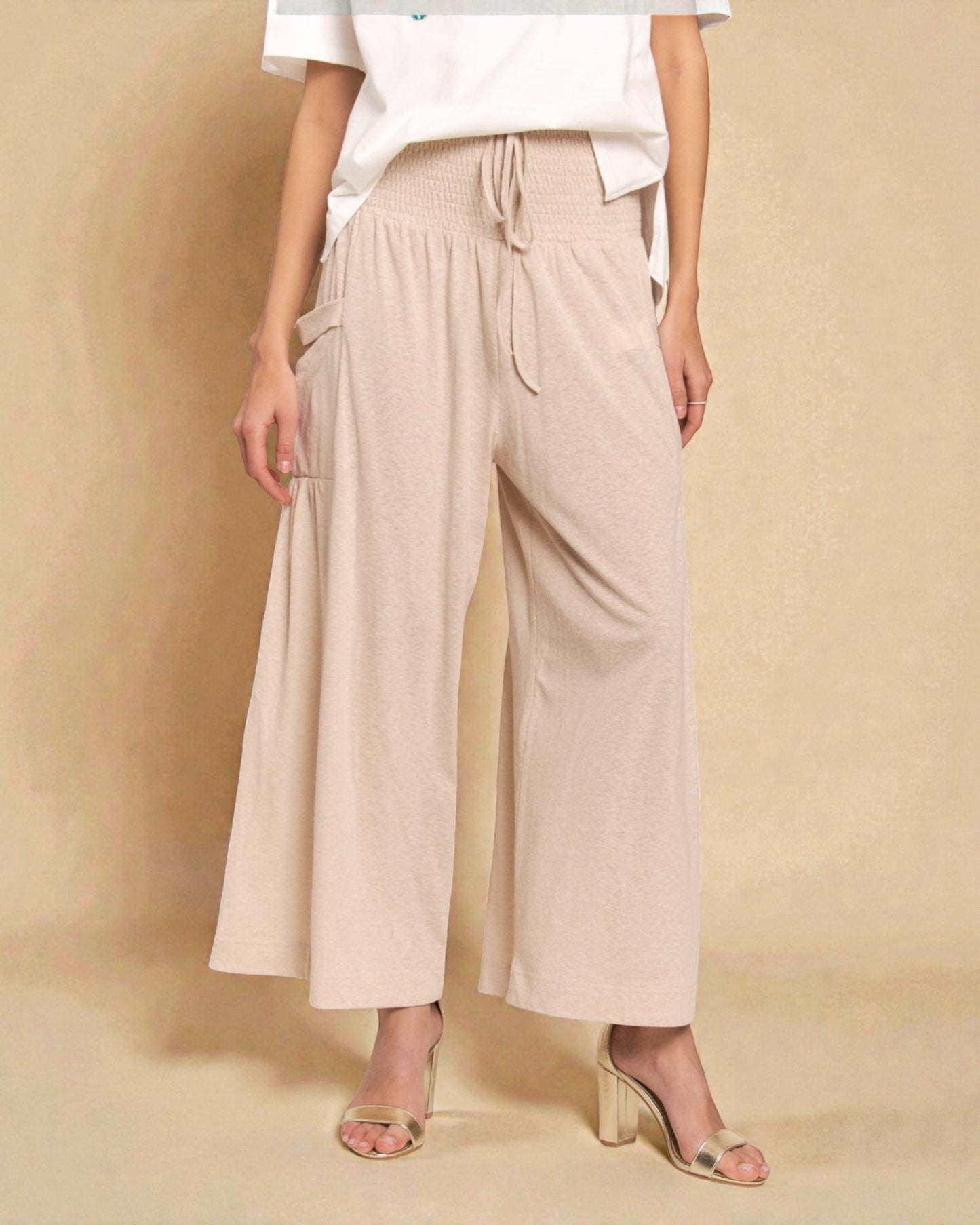 Person wearing beige wide-leg pants and a white top against a beige background