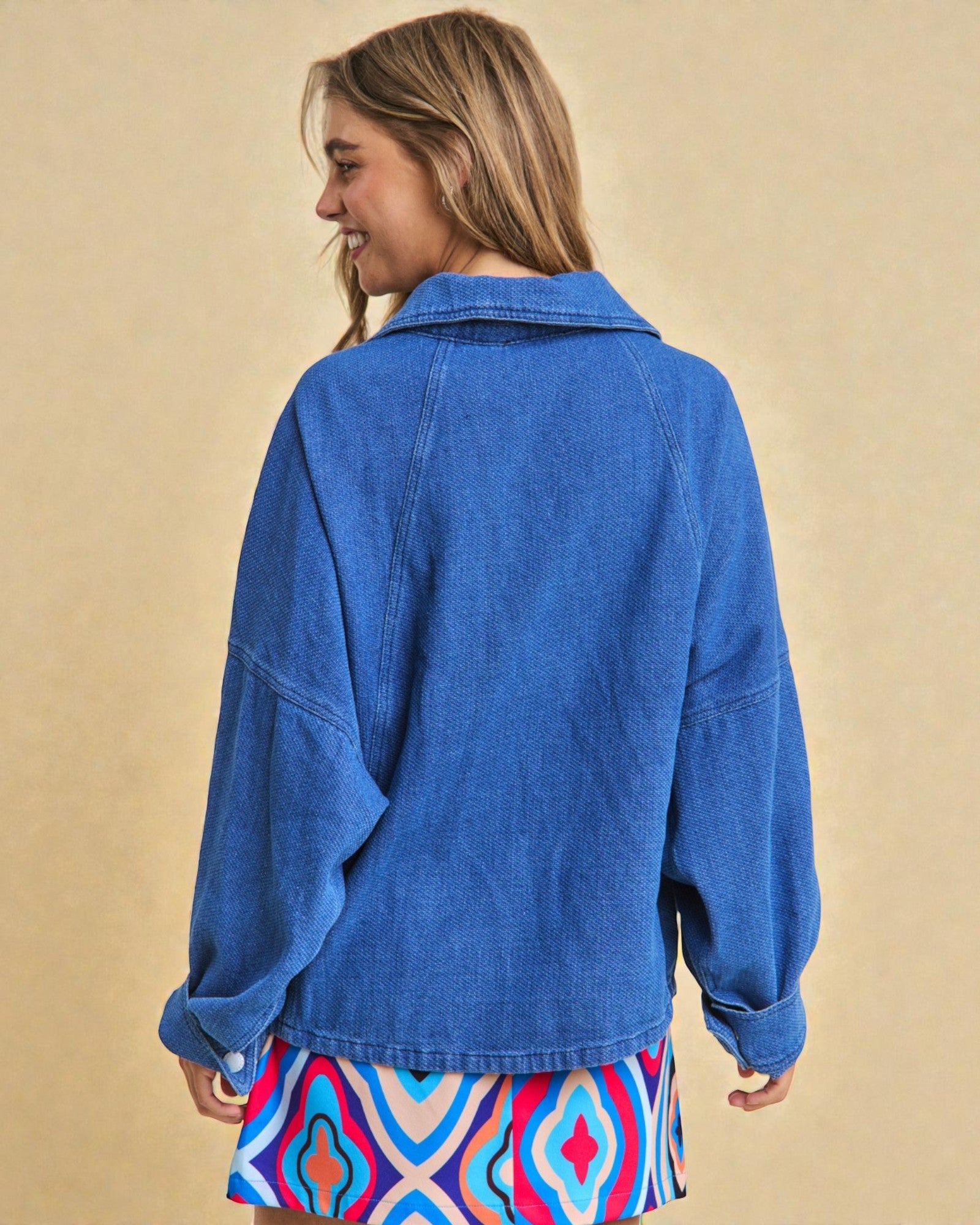 Person wearing a blue denim jacket with a beige background