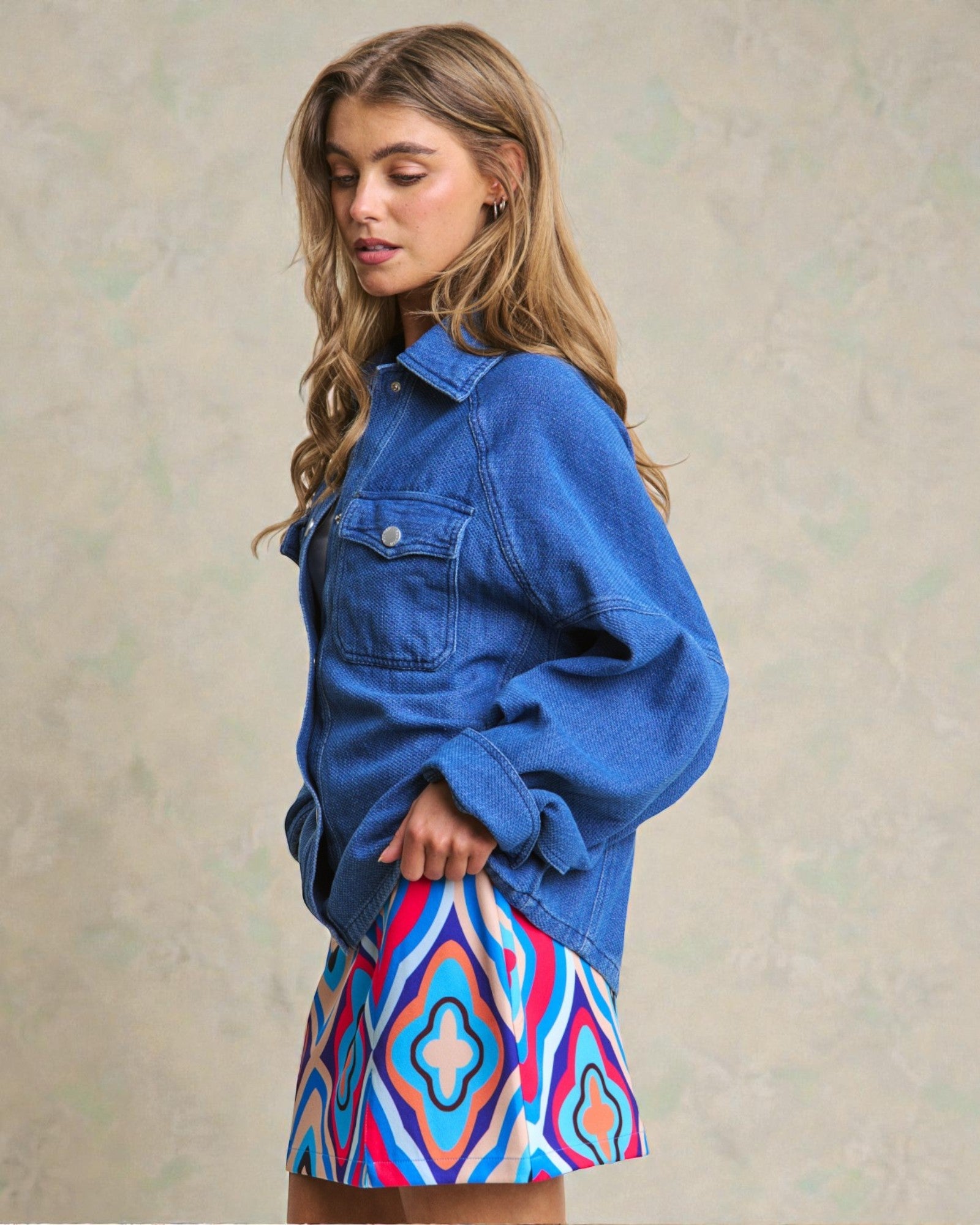 Woman wearing a blue denim jacket and colorful patterned skirt against a neutral background