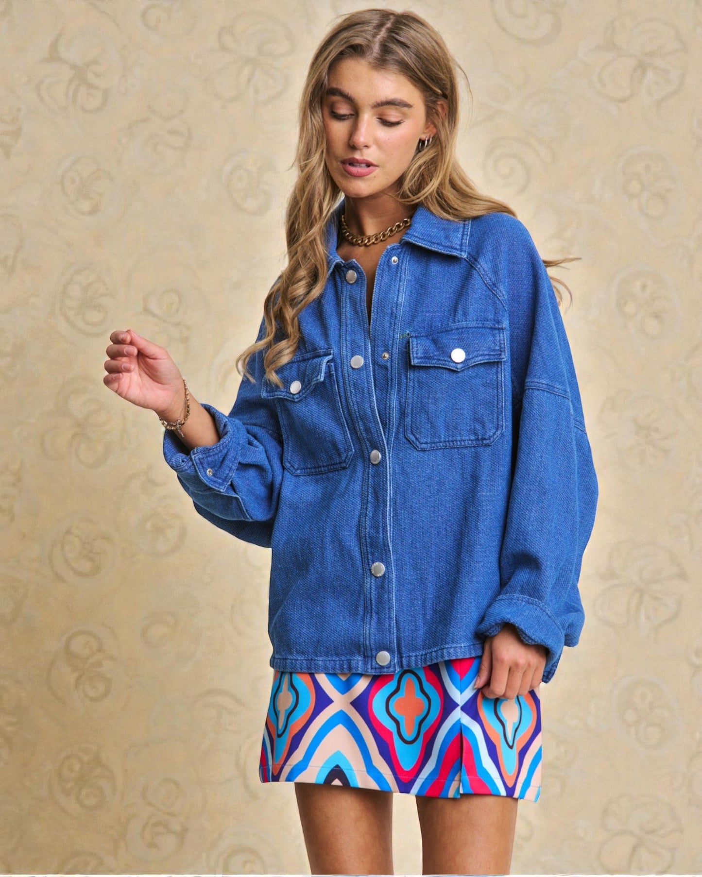 Woman wearing a blue denim jacket over a colorful dress on a beige patterned background